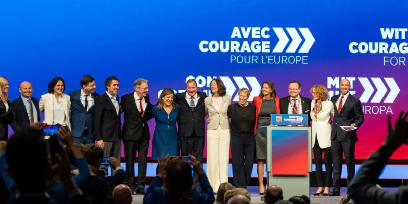 Na zdjęciu znajduje się grupa uśmiechniętych polityków na scenie podczas wydarzenia, z kolorowym tłem i hasłami promującymi wspólnotę europejską.