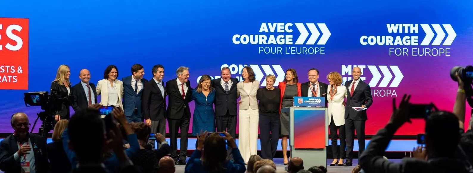 Na zdjęciu znajduje się grupa uśmiechniętych polityków na scenie podczas wydarzenia, z kolorowym tłem i hasłami promującymi wspólnotę europejską.