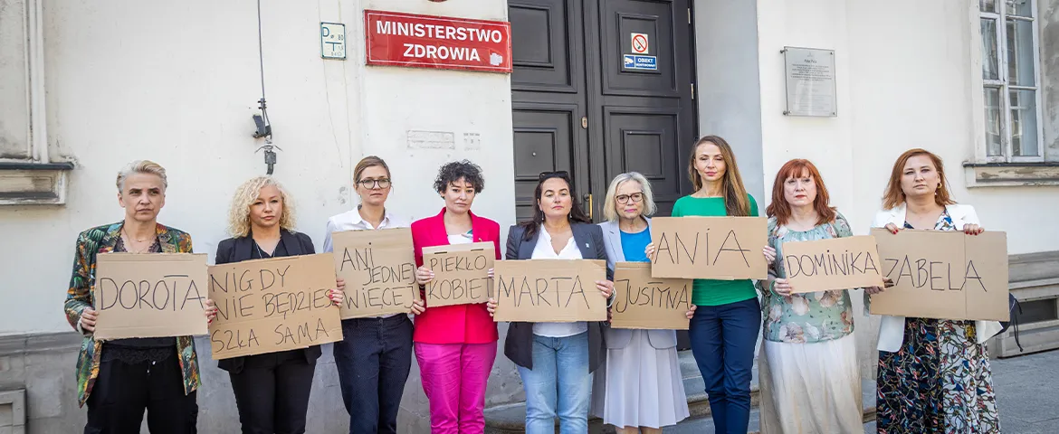 Grupa kobiet stoi przed wejściem do budynku Ministerstwa Zdrowia, trzymając kartonowe tabliczki z imionami i protestuje przeciwko drakońskiemu prawu antyaborcyjnemu w Polsce.
