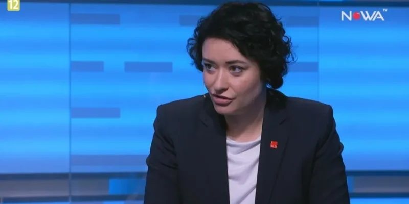 Kobieta w ciemnej marynarce i białej koszulce mówiąca w studiu telewizyjnym z niebieskim tłem i logiem stacji w prawym górnym rogu.