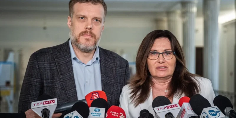 Dwoje osób podczas konferencji prasowej o WIBOR w wnętrzu budynku, kobieta z okularami po prawej, mężczyzna po lewej, otoczeni mikrofonami dziennikarzy.