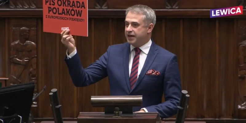 Polityk trzyma w ręku kartkę z napisem "PIS OKRADA POLAKÓW Z EUROPEJSKICH PIENIĘDZY!" podczas wystąpienia w Sejmie.