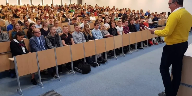 Prelegent stoi przy mównicy i przemawia do wypełnionej sali studentów podczas wykładu na Uniwersytecie Rzeszowskim.