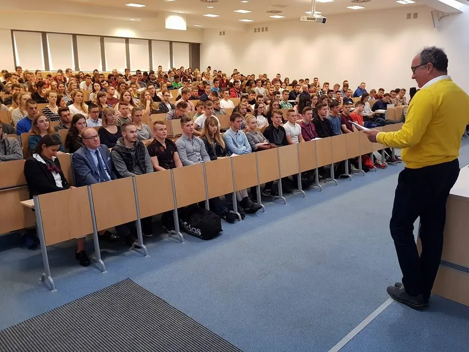 Prelegent stoi przy mównicy i przemawia do wypełnionej sali studentów podczas wykładu na Uniwersytecie Rzeszowskim.