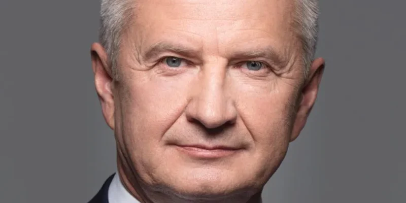 Portret mężczyzny w garniturze i niebieskim krawacie na neutralnym szarym tle, w kontekście debaty o przywróceniu obowiązkowego poboru wojskowego.