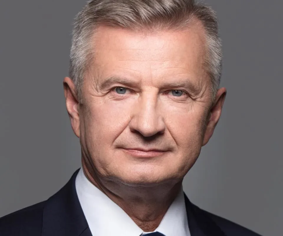 Portret mężczyzny w garniturze i niebieskim krawacie na neutralnym szarym tle, w kontekście debaty o przywróceniu obowiązkowego poboru wojskowego.