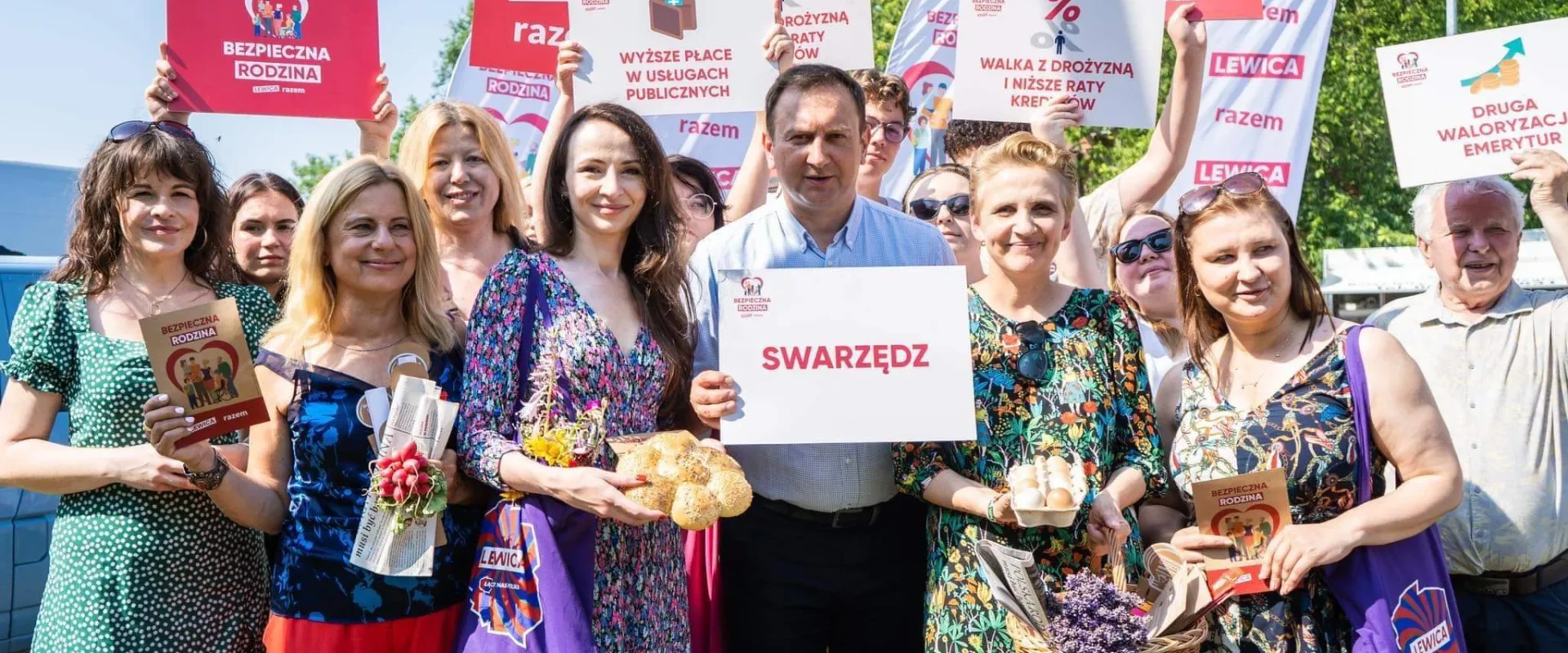 Grupa osób na zewnątrz podczas wydarzenia politycznego trzyma banery Lewicy i kartki z hasłami Bezpieczna Rodzina, a w centralnej części ktoś trzyma plakat z napisem Swarzędz; scena ilustruje obawy przed rekordową inflacją zagrażającą rodzinom.