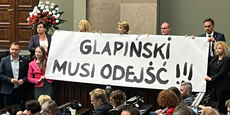 Na zdjęciu członkowie parlamentu trzymają transparent z hasłem "GLAPIŃSKI MUSI ODEJŚĆ" podczas posiedzenia.