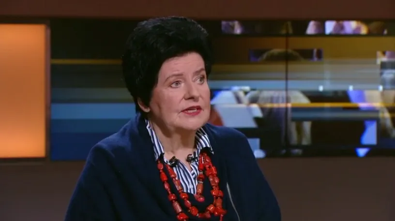 Kobieta o krótkich czarnych włosach, ubrana w ciemny żakiet i czerwony naszyjnik, przemawia w studiu telewizyjnym podczas rozmowy o szczepieniach.