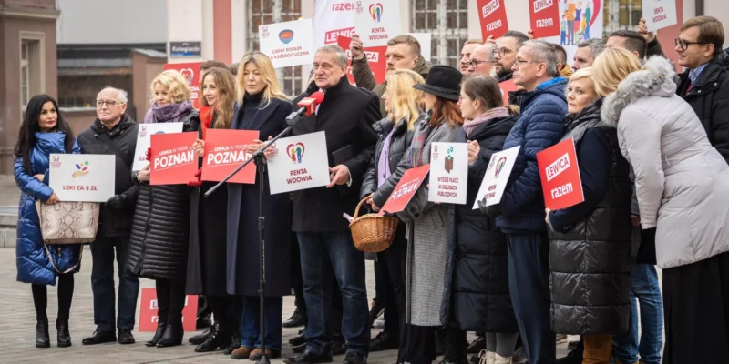 Grupa osób na demonstracji w Poznaniu trzyma plakaty z hasłem Lewica razem, a jeden mężczyzna przemawia do mikrofonu.