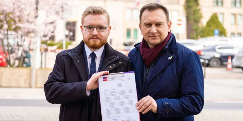 Dwóch mężczyzn trzymając wspólnie dokument, stoi na ulicy w tle z kwitnącymi drzewami.