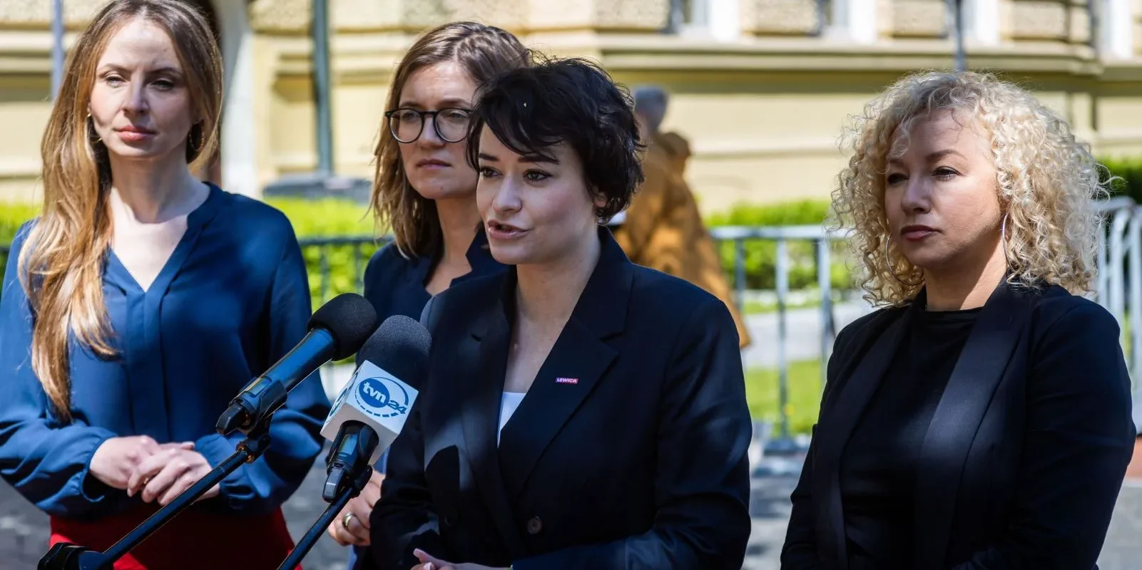 Na zdjęciu cztery kobiety stoją przy mikrofonach, jedna z nich przemawia, podczas konferencji prasowej na świeżym powietrzu.