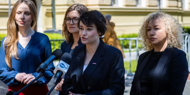Na zdjęciu cztery kobiety stoją przy mikrofonach, jedna z nich przemawia, podczas konferencji prasowej na świeżym powietrzu.