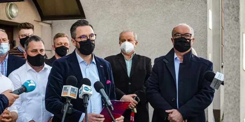 Grupa mężczyzn w maseczkach stoi przed mikrofonami podczas konferencji prasowej, a centralnie ustawiony mówca w granatowym garniturze mówi o otwartej, punktowej współpracy z Agronią.