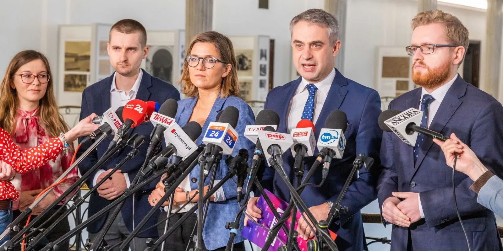 Konferencja prasowa z udziałem trzech mówców oraz przedstawicieli mediów, z mikrofonami skierowanymi w stronę mówiącego.