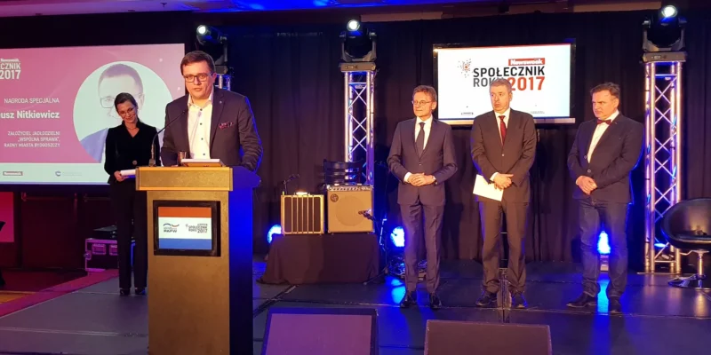 Mężczyzna przy mównicy odbiera nagrodę specjalną podczas gali "Społecznik Roku 2017", obok stoją trzy osoby i widoczne są ekrany z nazwą wydarzenia.
