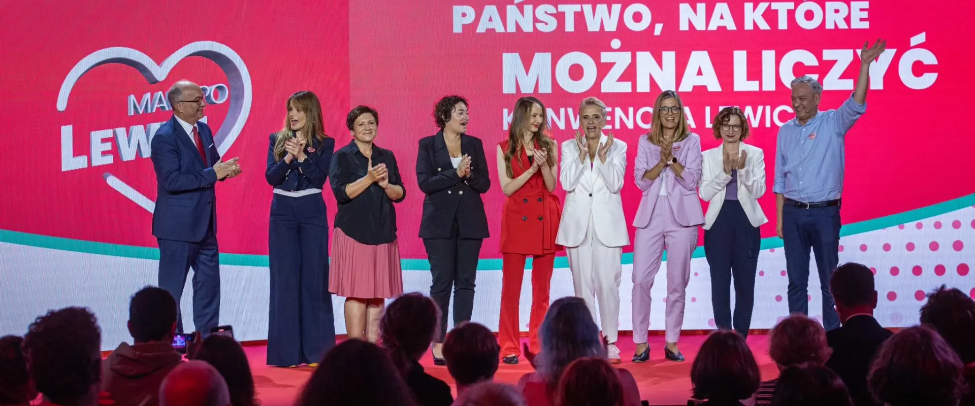Grupa polityków stoi na scenie podczas wydarzenia, klaszcze i uśmiecha się, na tle dużego różowo-czerwonego baneru z napisem „PAŃSTWO, NA KTÓRE MOŻNA LICZYĆ” i logiem Lewicy.