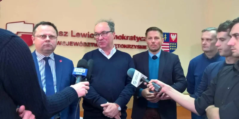 Kilku mężczyzn stoi na konferencji prasowej przed mikrofonami, z napisem i herbem na ścianie za nimi.