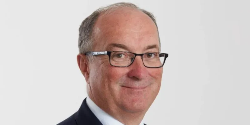 Uśmiechnięty mężczyzna w okularach na jasnym tle.