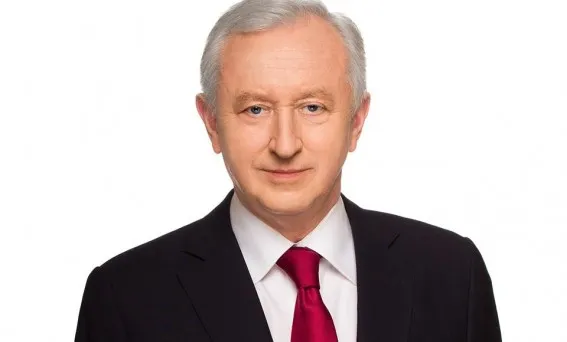 Portret starszego mężczyzny w ciemnym garniturze i bordowym krawacie na białym tle.