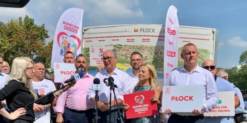 Na zdjęciu przedstawiono grupę osób trzymających transparenty w trakcie wydarzenia promującego bezpieczeństwo rodzin w Płocku.