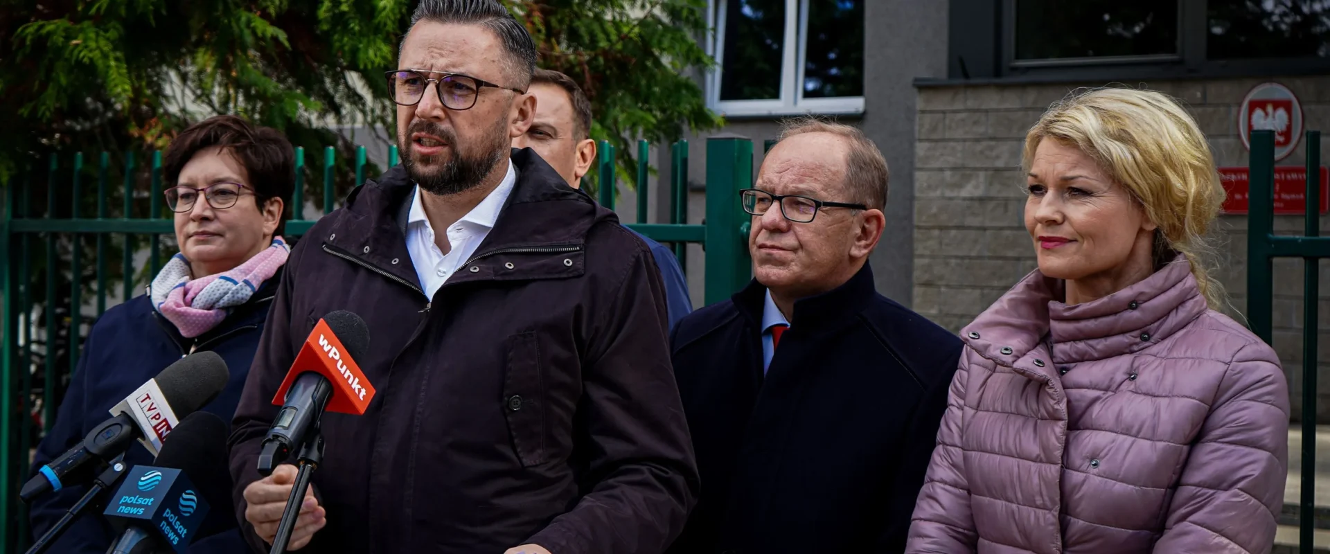 Grupa lokalnych działaczy i polityków wygłasza konferencję prasową przed budynkiem, broniąc społeczności lokalnych i podkreślając hasło „Nie ma demokracji bez samorządności”.