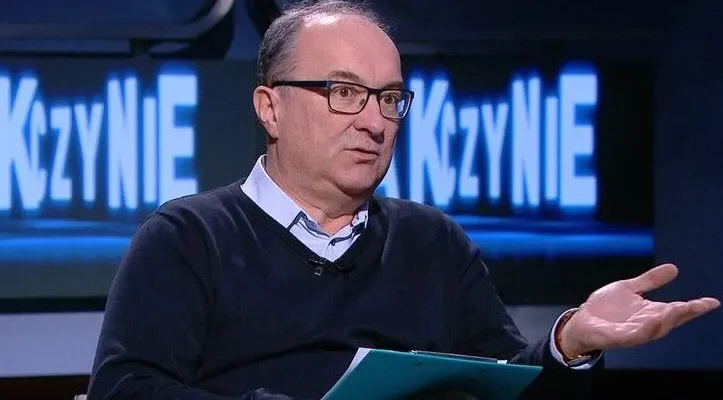 Osoba w okularach siedzi w studiu telewizyjnym, gestykuluje jedną dłonią i trzyma dokumenty podczas rozmowy o likwidacji IPN.