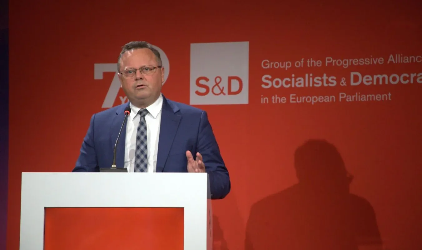 Mężczyzna w granatowym garniturze przemawia z mównicy na czerwonym tle z logo S&D oraz napisem o Grupie Socjalistów i Demokratów w Parlamencie Europejskim.