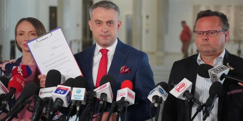 Grupa polityków Lewicy na konferencji prasowej domagającej się kontroli bonusów Polskiego Ładu; jeden z nich trzyma dokumenty przed licznymi mikrofonami.