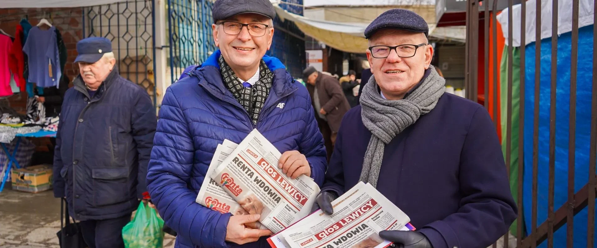 Dwóch starszych mężczyzn w czapkach i okularach trzyma gazety „Renta Wdowy” na targowisku w województwie pomorskim, będąc częścią kampanii Lewicy „Bezpieczna Rodzina”.
