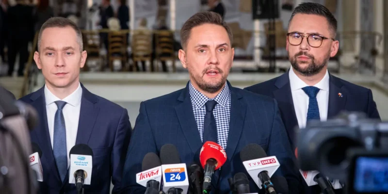 Trzech mężczyzn w garniturach stoi przed zestawem mikrofonów podczas konferencji prasowej dotyczącej wniosku o odwołanie przewodniczącego sejmowej Komisji Obrony Narodowej.