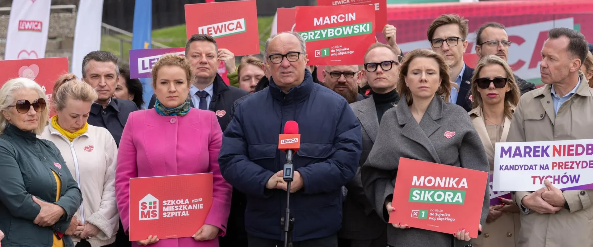Grupa polityków Lewicy podczas konferencji prasowej z plakatami wyborczymi i banerami z logo partii.
