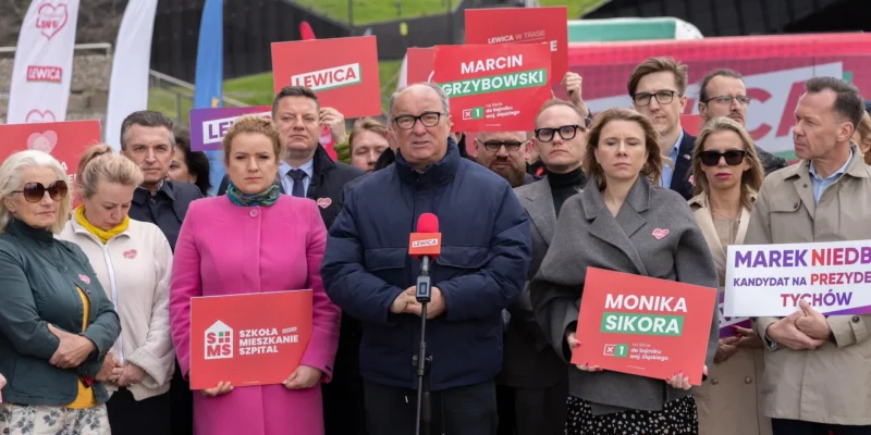 Grupa polityków Lewicy podczas konferencji prasowej z plakatami wyborczymi i banerami z logo partii.