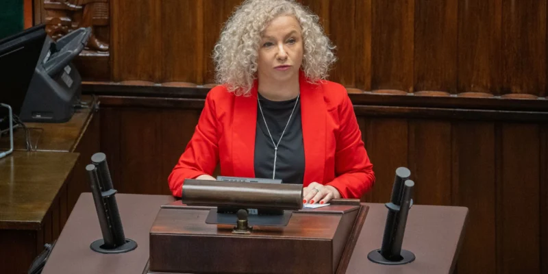 Kobieta o kręconych siwych włosach, ubrana w czerwoną marynarkę, siedzi za mównicą w sali obrad podczas debaty o aborcji.