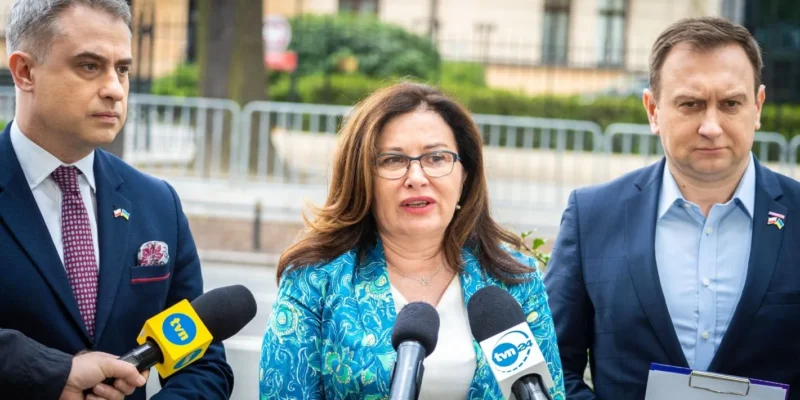 Na zdjęciu widoczni są trzej mówiący politycy, z mikrofonami, w otoczeniu zieleni w tle.