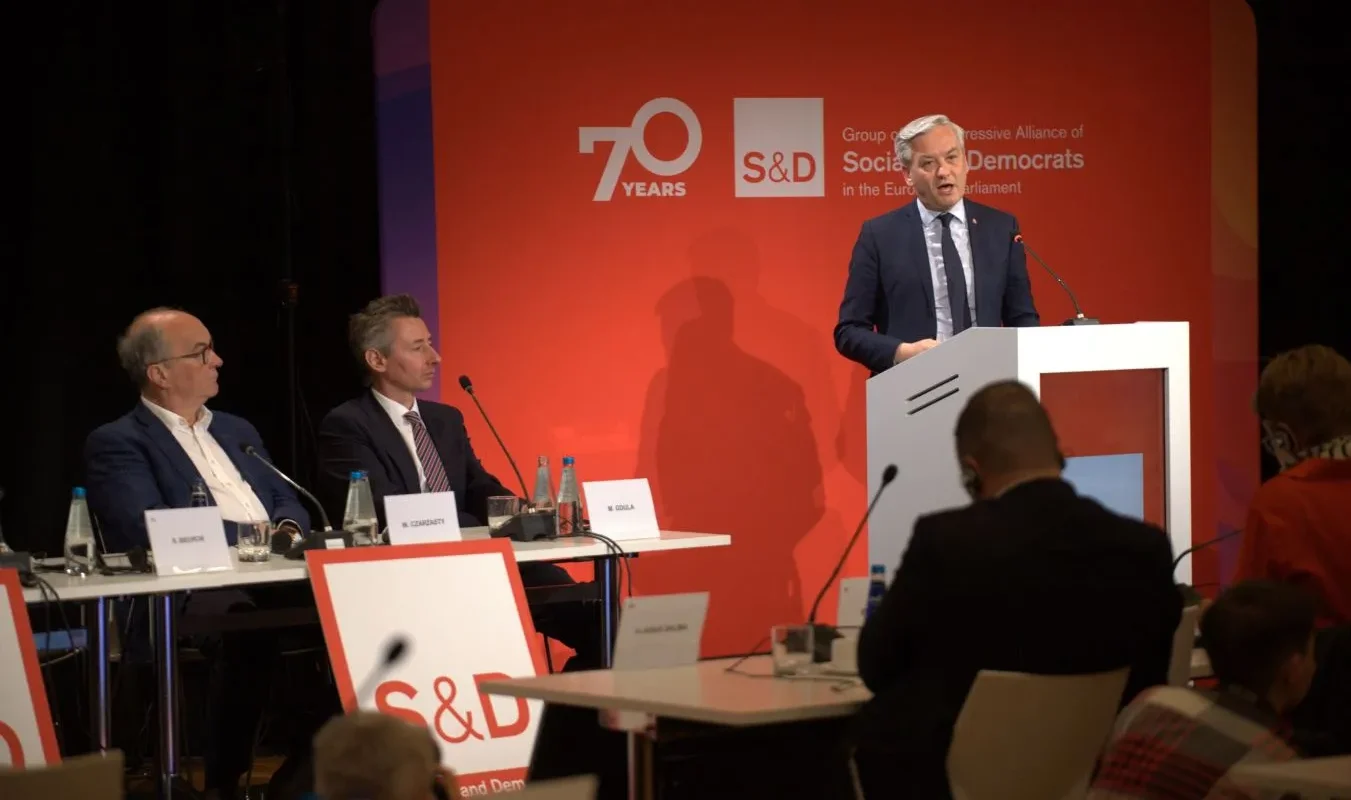 Mężczyzna w garniturze przemawia z mównicy podczas panelu konferencyjnego, na tle czerwonego banera z logo S&D i napisem „70 Years”, przy stole siedzą inni paneliści.