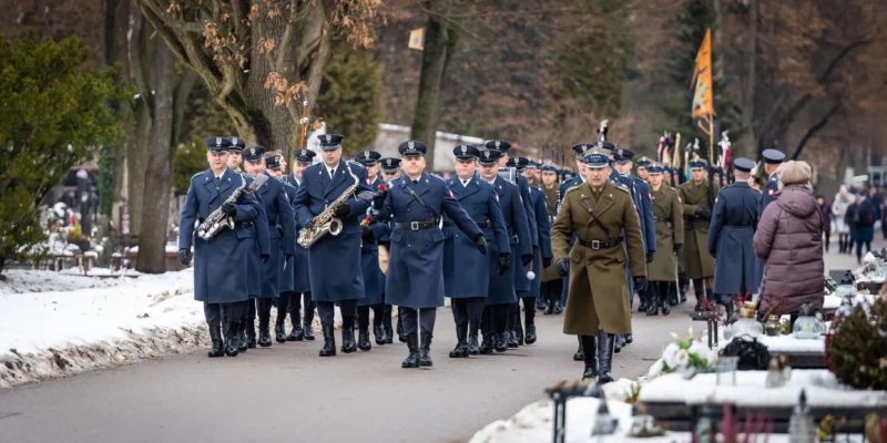 Na zdjęciu widać mundurowych mężczyzn i kobiet w czasie ceremonii, maszerujących cmentarną alejką w zimowej scenerii.