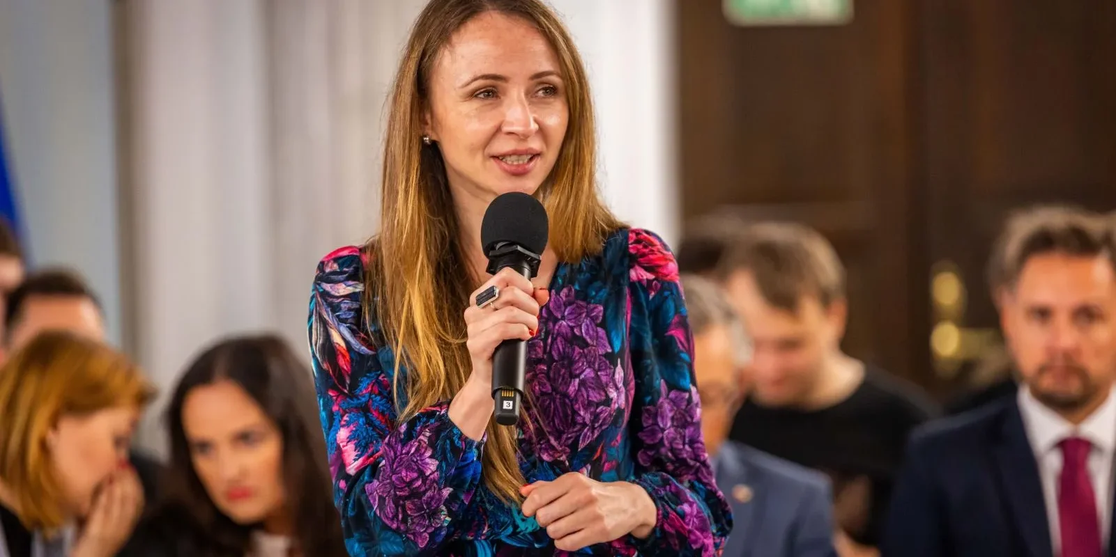 Kobieta przemawia do mikrofonu podczas konferencji o podwyżkach dla nauczycieli, w tle siedzą inni uczestnicy.