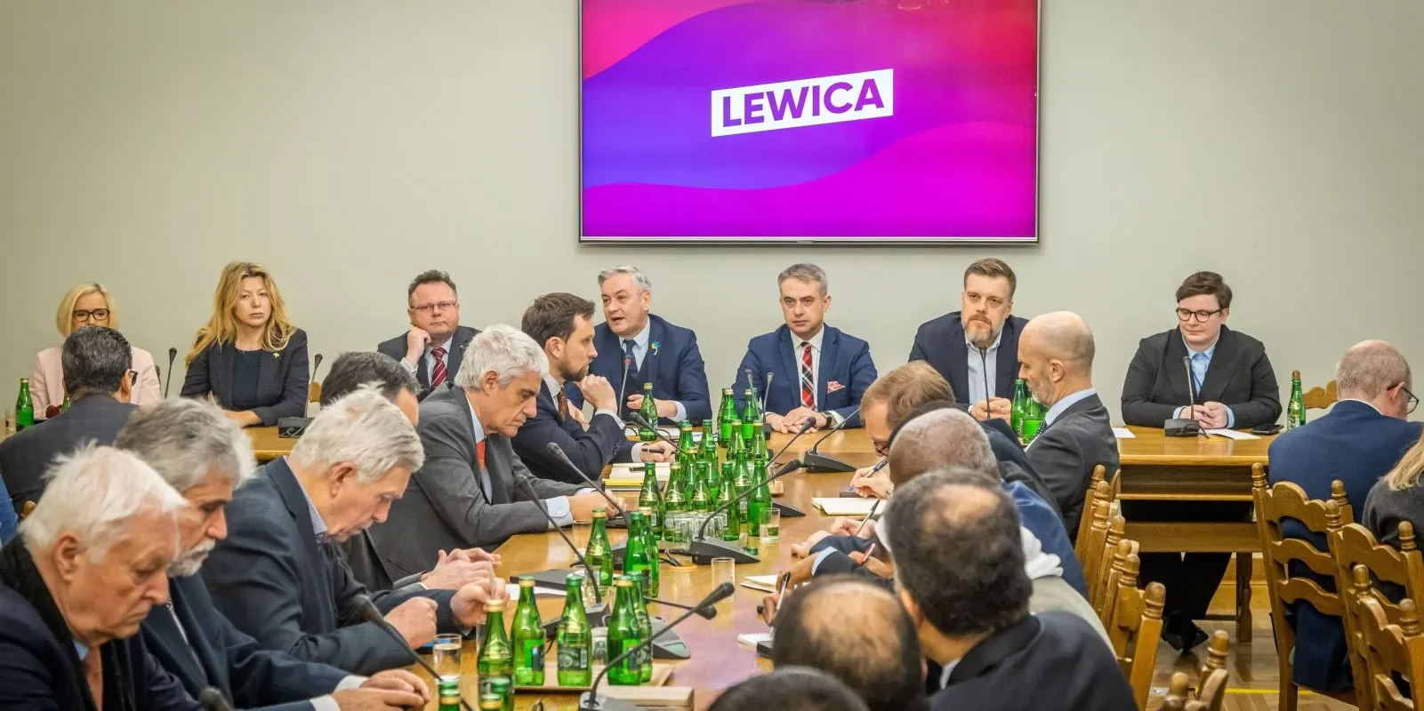 Zdjęcie przedstawia spotkanie grupy osób siedzących przy stole, z widocznym napisem "LEWICA" na ekranie w tle.