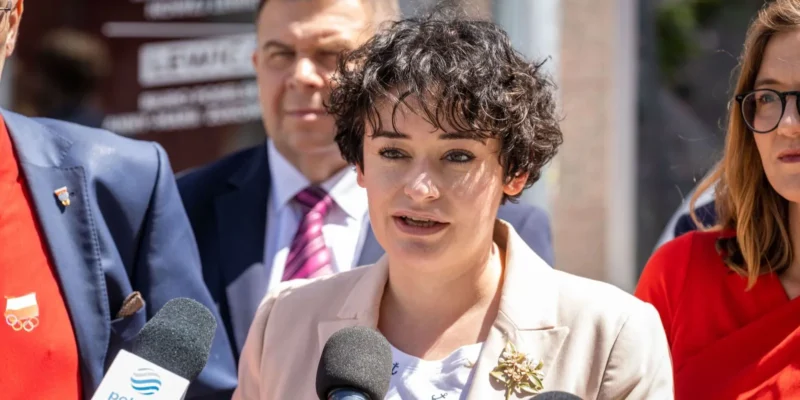 Kobieta o krótkich kręconych włosach w beżowym żakiecie przemawia do mikrofonów podczas konferencji prasowej o Funduszu Sprawiedliwości; w tle stoją inni politycy.