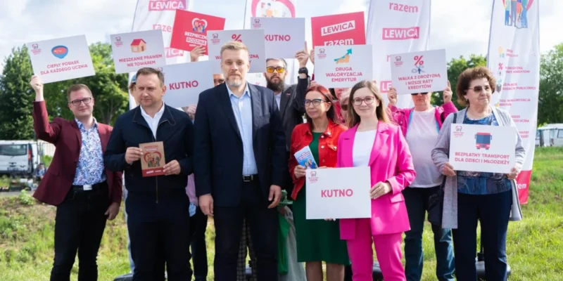 Grupa zwolenników Lewicy podczas plenerowego wydarzenia trzyma plakaty i banery z logo partii, a w pierwszym planie widoczny jest plakat z napisem „KUTNO”.