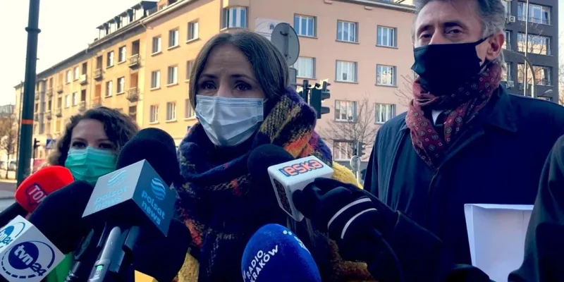 Trzy osoby w maseczkach stojące przed zestawem mikrofonów dziennikarzy podczas konferencji prasowej na zewnątrz budynku Małopolskiego Kuratorium Oświaty podczas kontroli poselskiej.