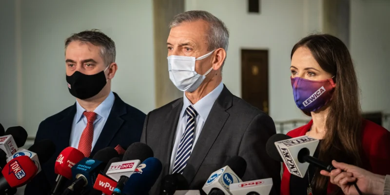 Trzy osoby w garniturach i maseczkach stojące przy licznych mikrofonach podczas konferencji prasowej w sprawie powołania Parlamentarnego Zespołu ds. nauczycielek i nauczycieli oraz pracowników oświaty.