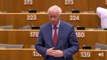 Mężczyzna w garniturze i czerwonym krawacie stoi przy mównicy w sali obrad Parlamentu Europejskiego podczas debaty o pakiecie dotyczącym mobilności.