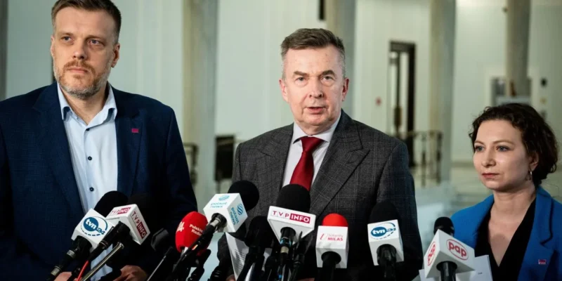 Na zdjęciu trzech polityków stoi przed mikrofonami w budynku, najprawdopodobniej podczas konferencji prasowej.