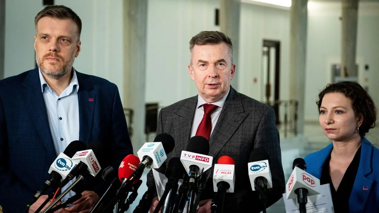 Na zdjęciu trzech polityków stoi przed mikrofonami w budynku, najprawdopodobniej podczas konferencji prasowej.