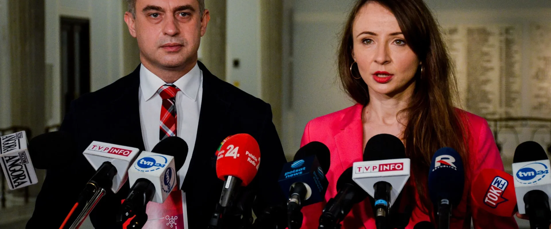 Dwóch polityków podczas konferencji prasowej, otoczonych licznymi mikrofonami mediów, omawia temat czwartej fali koronawirusa.