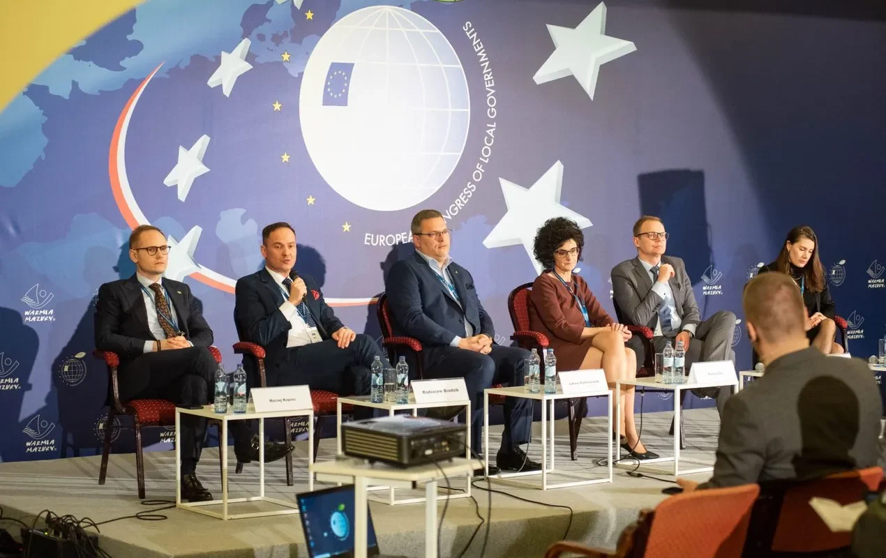 Na zdjęciu przedstawiono panel dyskusyjny z udziałem kilku mówców na tle grafiki związanej z Europejskim Kongresem Samorządów.