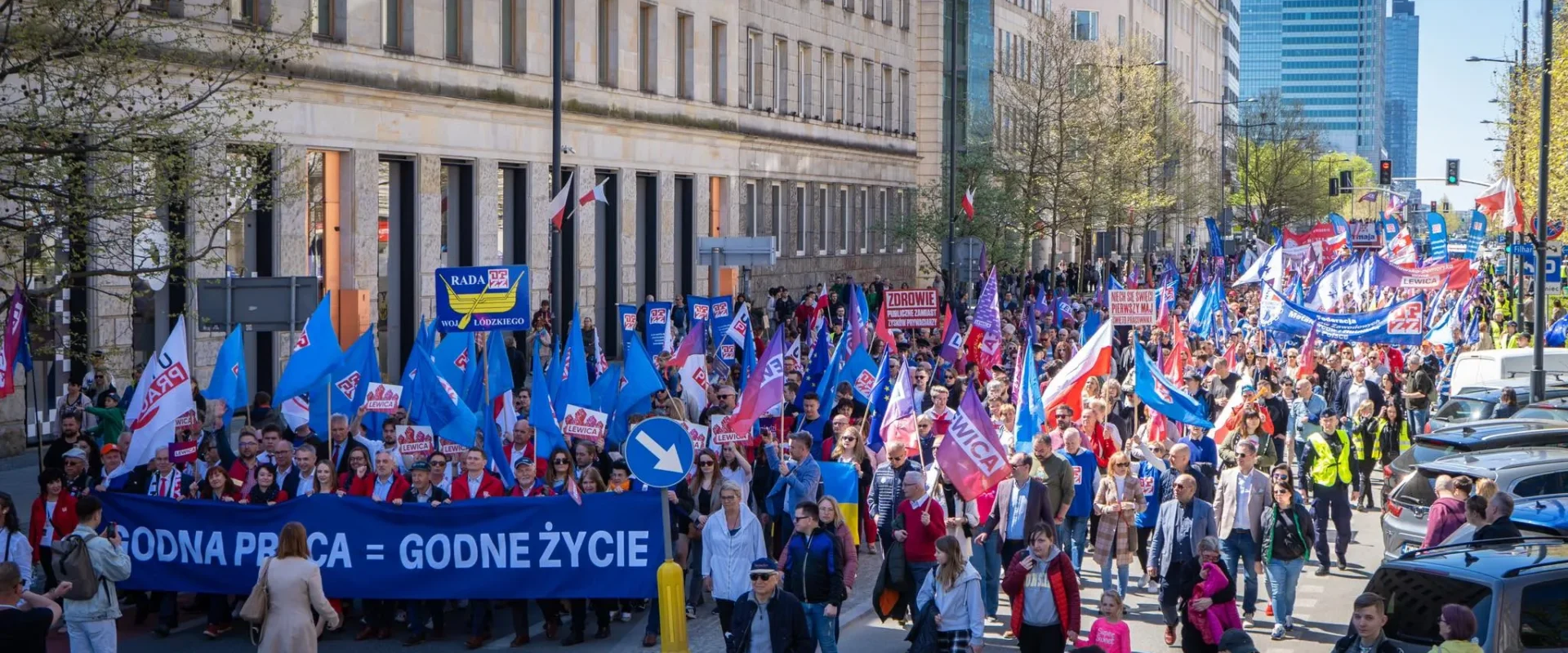 Tłumaczony marsz z transparentami i flagami, podczas którego uczestnicy wyrażają swoje postulaty dotyczące pracy i życia.