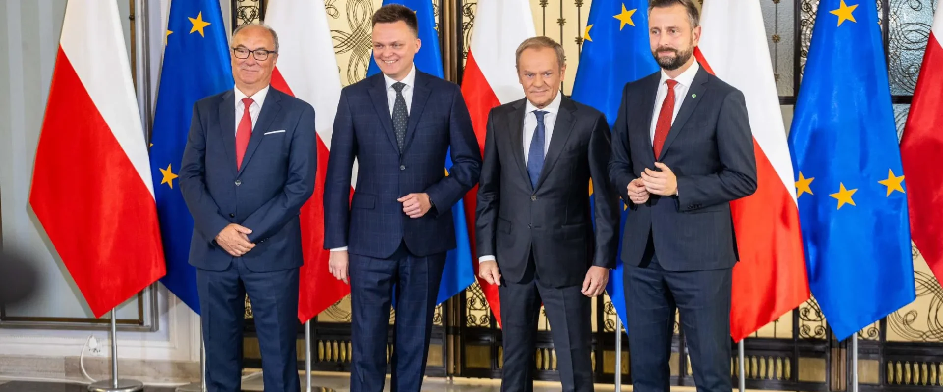 Czterech mężczyzn w garniturach stoi przed flagami Polski i Unii Europejskiej, prezentując wspólne oświadczenie opozycji.